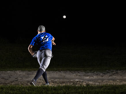Junger Mann mit Sportkleidung wirft Baseball bei Nacht - STSF03748