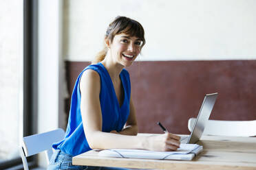 Happy businesswoman sitting with laptop at desk - EBSF03552