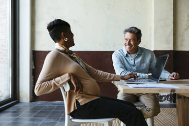 Happy businessman sitting with colleague at desk - EBSF03556