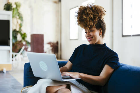 Happy businesswoman using laptop on sofa in office - EBSF03574