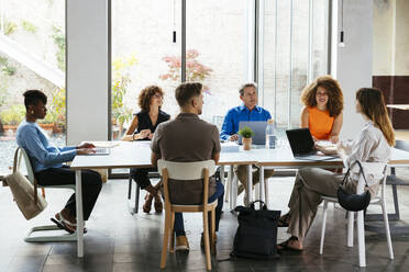 Businessmen and businesswomen discussing at desk - EBSF03586