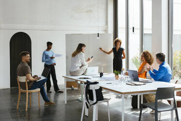 Businesswoman standing by whiteboard and having discussion with colleagues - EBSF03601