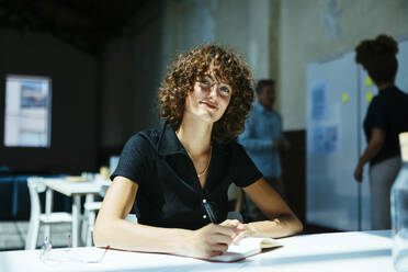 Lächelnde junge Geschäftsfrau sitzt mit Tagebuch im Büro - EBSF03622