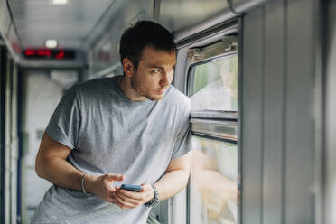 Man holding smart phone leaning on window of railroad car - VSNF01089