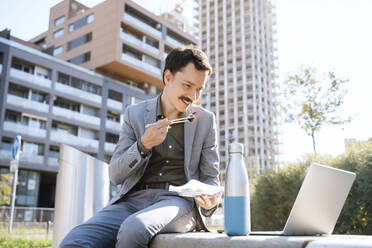 Businessman having lunch and video calling on laptop sitting at office park - NDEF00770