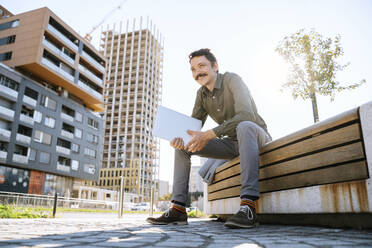 Smiling thoughtful businessman with laptop sitting on bench at office park - NDEF00777