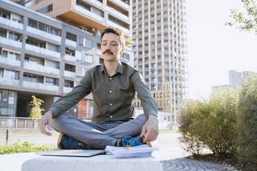 Businessman meditating sitting cross-legged at office park - NDEF00779