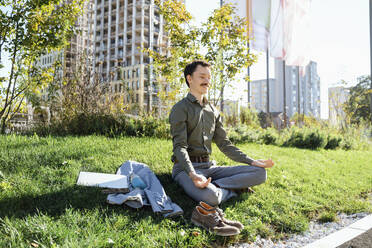 Businessman meditating sitting on grass at office park - NDEF00781