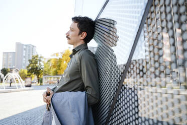 Thoughtful businessman leaning on modern office building - NDEF00787