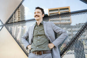 Smiling businessman with arms akimbo standing in front of modern office building - NDEF00798