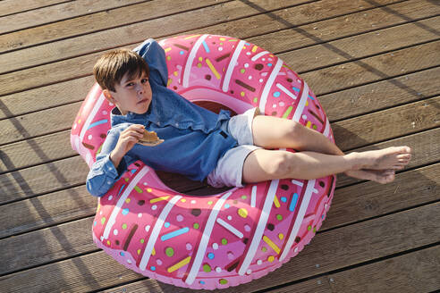 Boy with snack lying on inflatable swim ring - ASGF03831