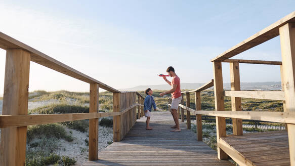 Vater und Sohn spielen auf der Strandpromenade mit einem Spielzeugflugzeug - ASGF03835