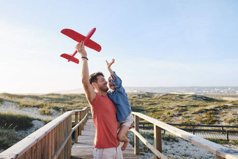 Glücklicher Vater und Sohn spielen mit Spielzeugflugzeug an einem sonnigen Tag - ASGF03838