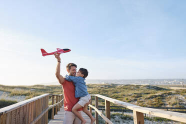 Glücklicher Sohn und Vater spielen mit Spielzeugflugzeug an einem sonnigen Tag - ASGF03839