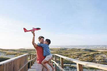 Happy son and father playing with toy airplane on sunny day - ASGF03839