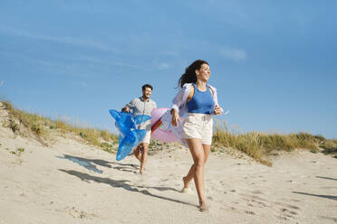 Glückliche Frau mit Mann läuft am Strand an einem sonnigen Tag - ASGF03851