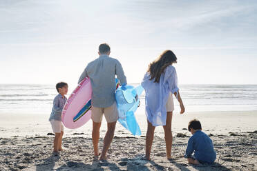Familie mit aufblasbarem Schwimmring und Spielzeug-Hai am Strand an einem sonnigen Tag - ASGF03856