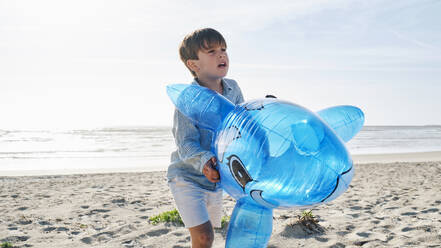 Junge mit aufblasbarem Spielzeug-Hai an einem sonnigen Tag am Strand - ASGF03866