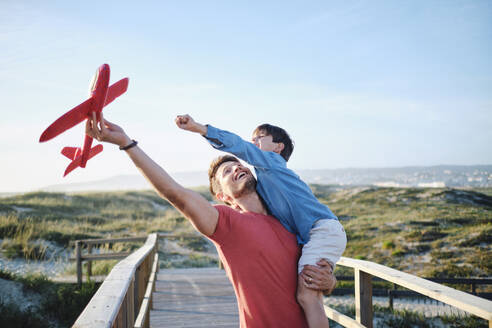 Happy father and son playing with toy airplane on sunny day - ASGF03874