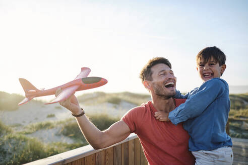 Glücklicher Junge mit Vater, der ein Spielzeugflugzeug hält und sich an einem sonnigen Tag amüsiert - ASGF03876