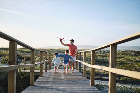 Vater hält Spielzeugflugzeug mit Kindern, die auf der Strandpromenade rennen und Spaß haben - ASGF03877