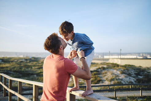 Father embracing son standing on wooden railing - ASGF03882