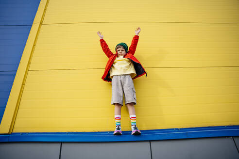 Boy with arms raised standing in front of yellow wall - MDOF01351