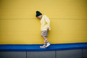 Junge mit Sweatshirt geht an gelber Wand vorbei - MDOF01360