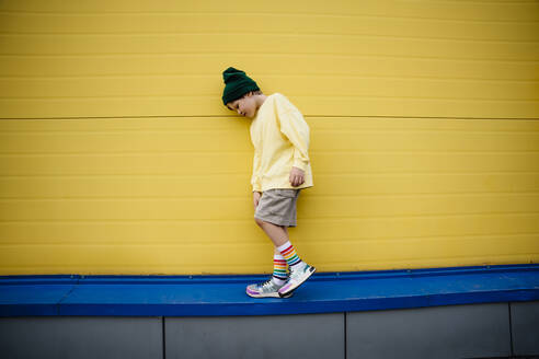 Boy wearing sweatshirt walking by yellow wall - MDOF01360