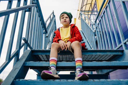 Thoughtful boy in red jacket sitting on metallic staircase - MDOF01365