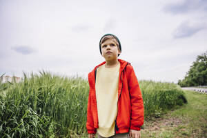 Junge mit roter Jacke steht neben Gerste auf einem Feld - MDOF01370