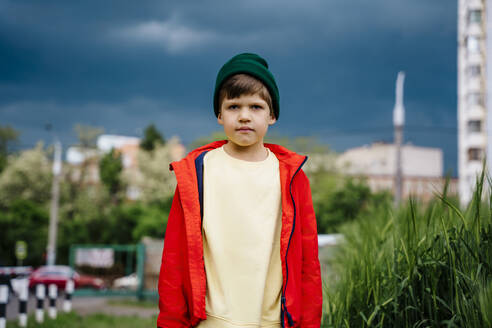 Junge in roter Jacke steht auf einem Feld mit bewölktem Himmel im Hintergrund - MDOF01375