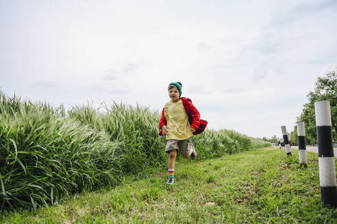 Junge mit roter Jacke, der durch die Gerstenernte auf einem Feld läuft - MDOF01381