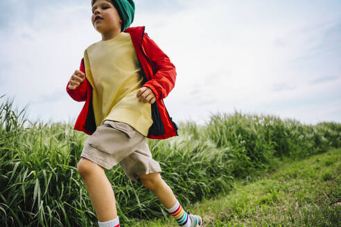 Boy in red jacket running by barley crop on field - MDOF01382