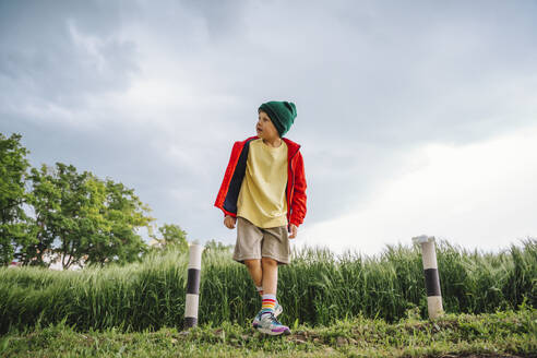 Junge in roter Jacke steht inmitten von Pollern auf einem Gerstenfeld - MDOF01389