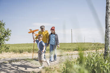 Glücklicher Junge und Mädchen gehen mit Großvater an einem sonnigen Tag spazieren - UUF28933