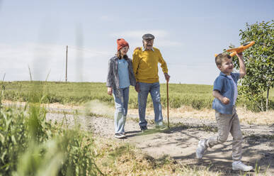 Happy girl and boy with grandfather walking on road - UUF28934