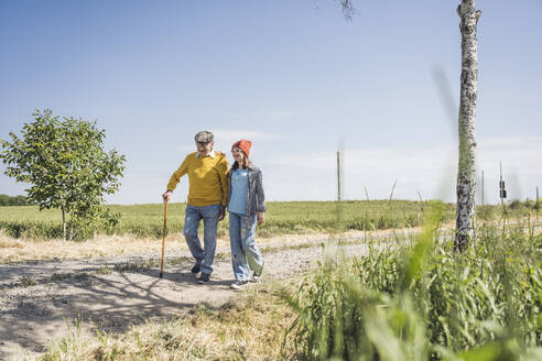 Happy girl walking with grandfather on road - UUF28935