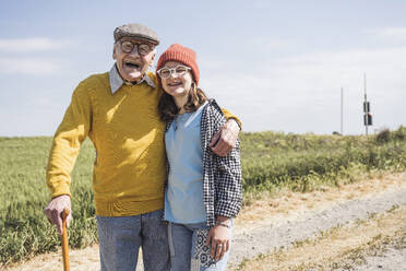 Cheerful senior man standing with granddaughter on dirt road - UUF28944