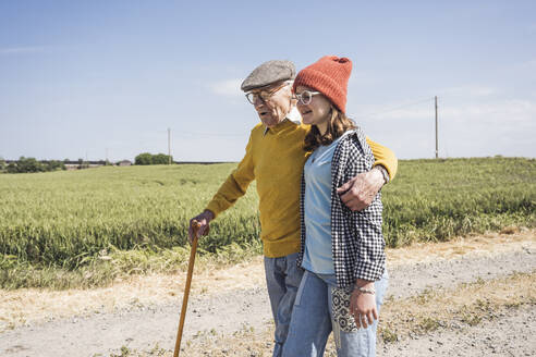 Smiling girl walking with grandfather on road - UUF28945