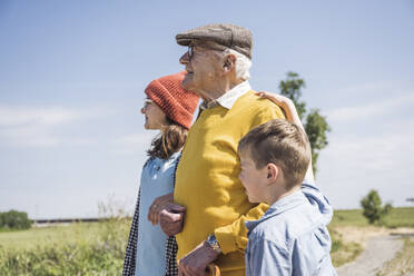 Älterer Mann steht mit Enkelin und Enkel an einem sonnigen Tag - UUF28951