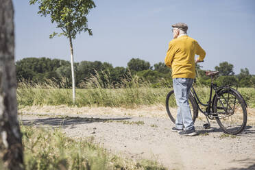 Aktiver älterer Mann zu Fuß mit Fahrrad auf der Straße - UUF28955