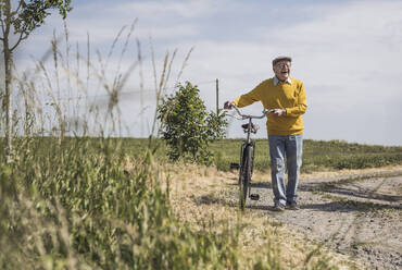 Happy senior man walking with bicycle on road - UUF28956