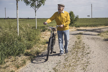 Happy senior man walking with bicycle on sunny day - UUF28957