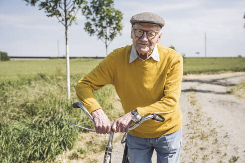 Lächelnder älterer Mann mit Fahrrad an einem sonnigen Tag - UUF28958