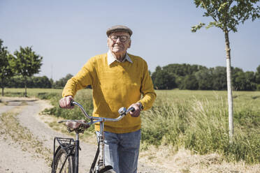 Smiling senior man walking with bicycle on sunny day - UUF28959