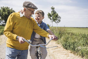 Happy senior man with grandson sitting on bicycle - UUF28961