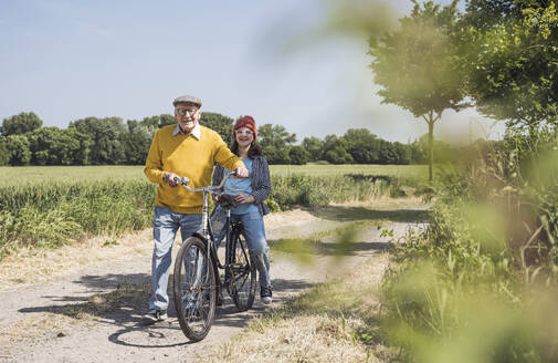 Glücklicher älterer Mann mit Enkelin auf dem Fahrrad sitzend - UUF28968