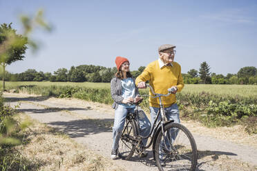 Lächelnder älterer Mann mit Enkelin auf dem Fahrrad sitzend - UUF28969