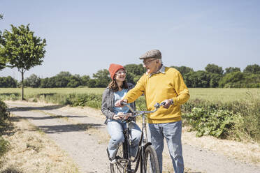 Happy grandfather with granddaughter sitting on bicycle at field - UUF28971